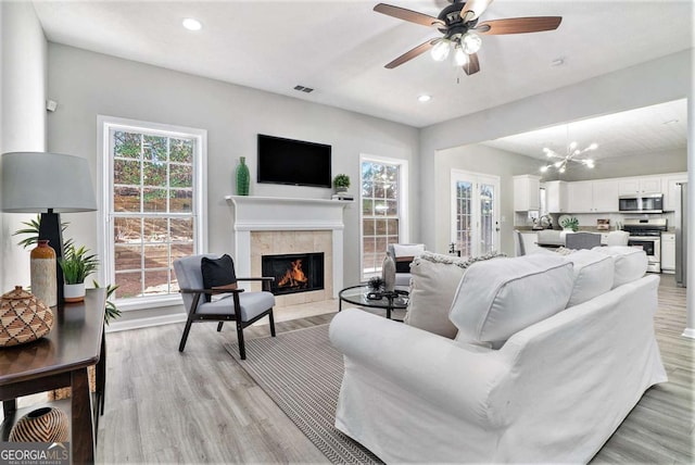 living room featuring visible vents, light wood finished floors, a tiled fireplace, and a wealth of natural light