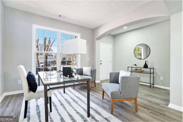 home office featuring arched walkways, wood finished floors, visible vents, and baseboards