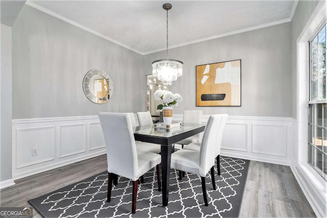 dining space with dark wood-style floors, a chandelier, ornamental molding, and a decorative wall