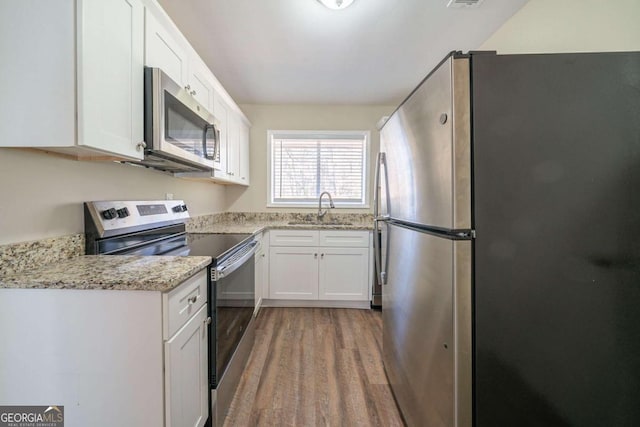 kitchen featuring light stone counters, wood finished floors, a sink, white cabinetry, and appliances with stainless steel finishes