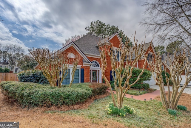 traditional home with brick siding, a shingled roof, concrete driveway, an attached garage, and fence