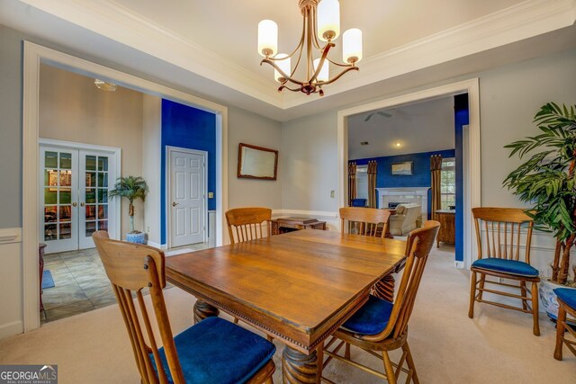 dining area featuring french doors, crown molding, a fireplace, a raised ceiling, and light carpet