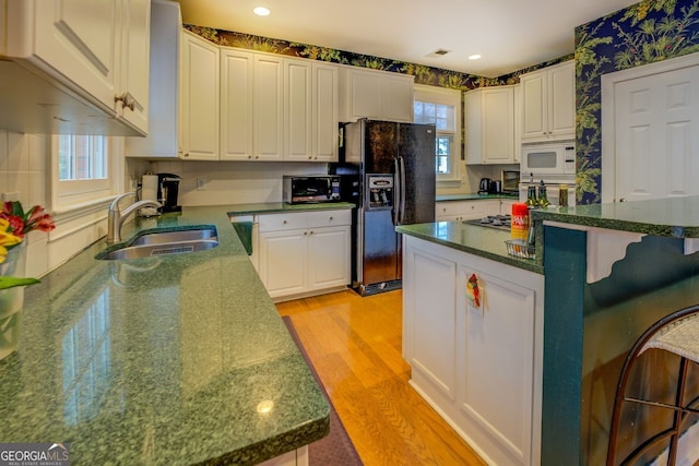 kitchen featuring a sink, light wood-style floors, white cabinets, black appliances, and wallpapered walls