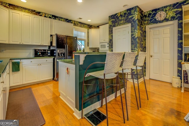 kitchen with wallpapered walls, white cabinets, dark countertops, light wood-style floors, and black fridge