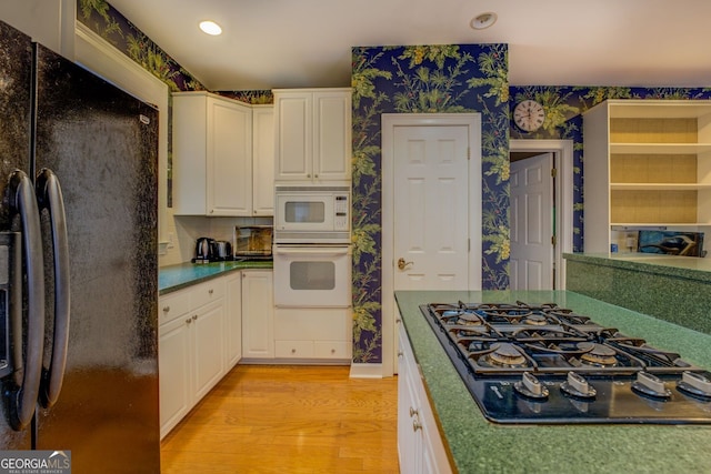 kitchen with wallpapered walls, light wood-style floors, dark countertops, black appliances, and white cabinetry