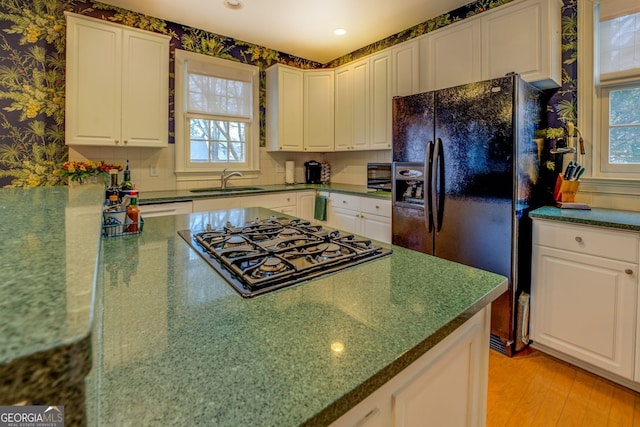 kitchen featuring light wood finished floors, white cabinets, a sink, black appliances, and wallpapered walls