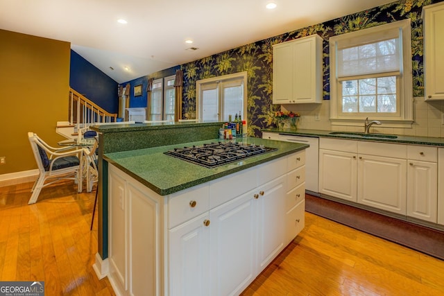 kitchen with black gas cooktop, light wood-type flooring, dark countertops, and a sink