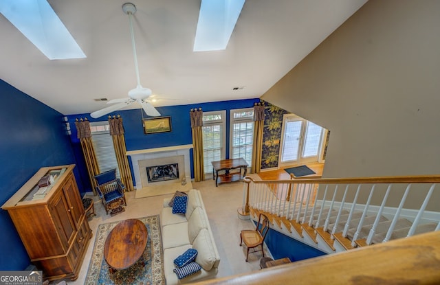 living area featuring vaulted ceiling with skylight, a fireplace, visible vents, a ceiling fan, and stairs