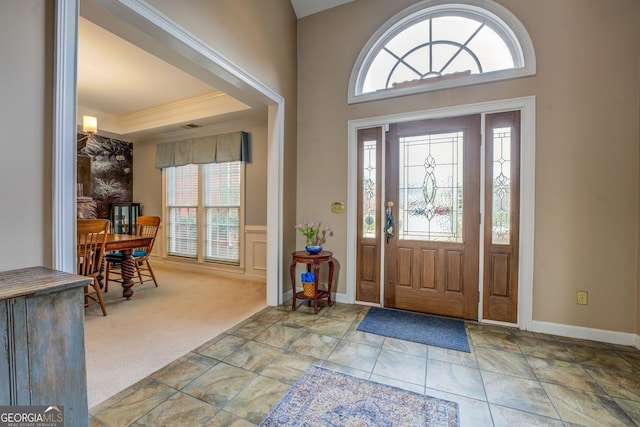 carpeted entrance foyer with baseboards and crown molding