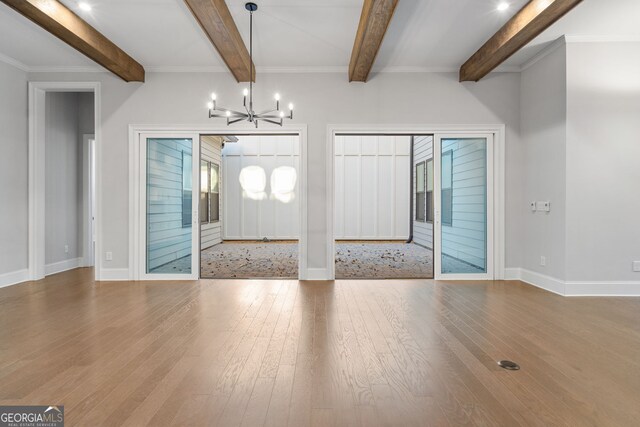 unfurnished dining area featuring beam ceiling, a notable chandelier, baseboards, and wood finished floors