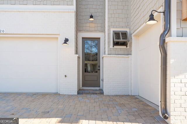 view of exterior entry with an attached garage and a wall unit AC