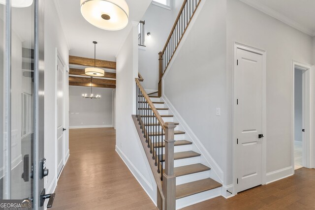 stairway featuring a chandelier, beamed ceiling, baseboards, and wood finished floors