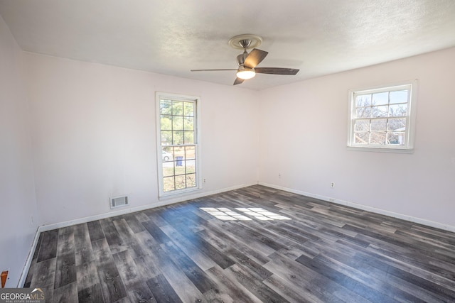 spare room featuring baseboards, a ceiling fan, visible vents, and dark wood-style floors