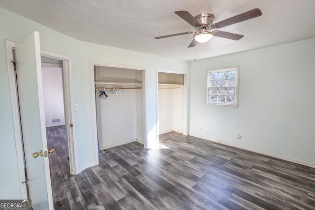 unfurnished bedroom with baseboards, visible vents, two closets, ceiling fan, and dark wood-type flooring