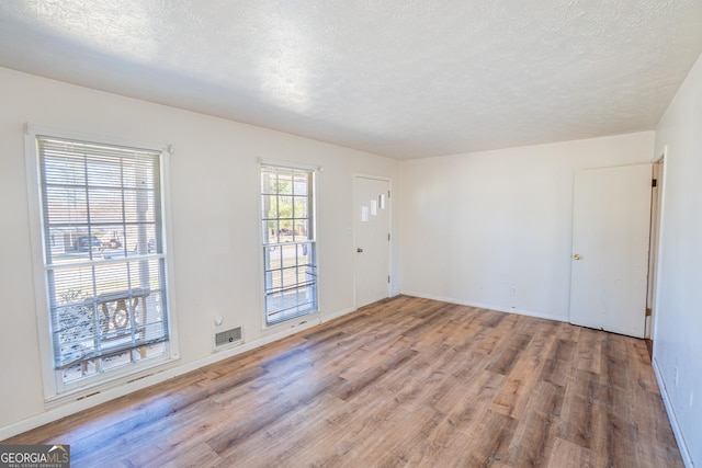 empty room with baseboards, a textured ceiling, visible vents, and wood finished floors