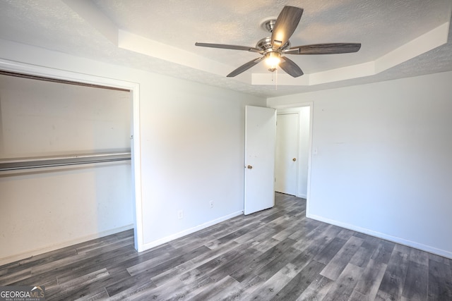 unfurnished bedroom with a tray ceiling, a textured ceiling, baseboards, wood finished floors, and a closet
