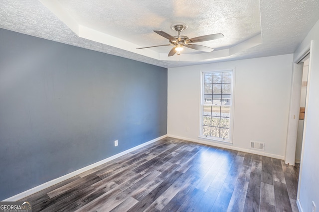 unfurnished bedroom featuring a tray ceiling, visible vents, baseboards, a textured ceiling, and dark wood-style flooring