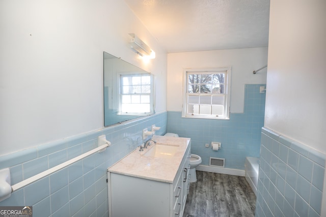 bathroom featuring toilet, tile walls, visible vents, wood finished floors, and vanity