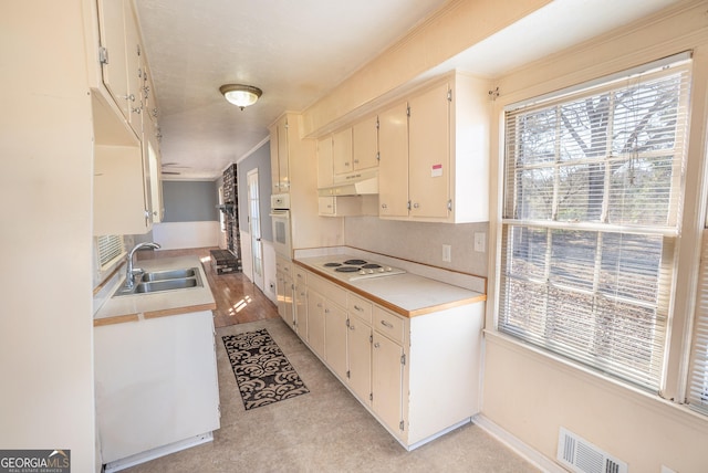 kitchen featuring a sink, white appliances, light countertops, under cabinet range hood, and visible vents