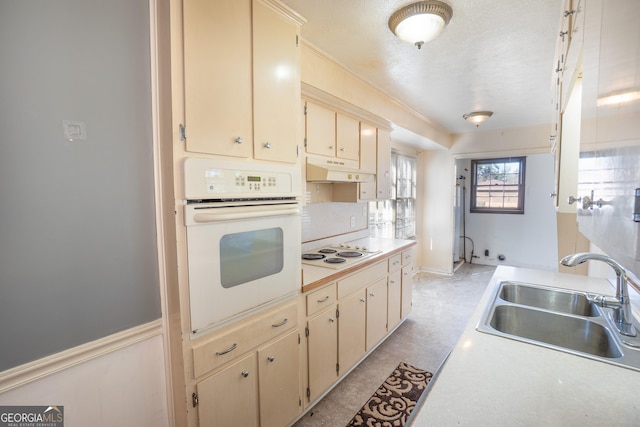 kitchen with a sink, white appliances, light countertops, under cabinet range hood, and cream cabinets