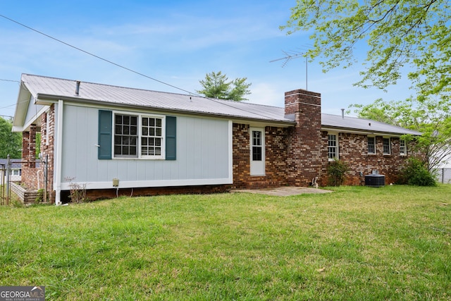 rear view of property with central air condition unit, brick siding, a chimney, and a lawn