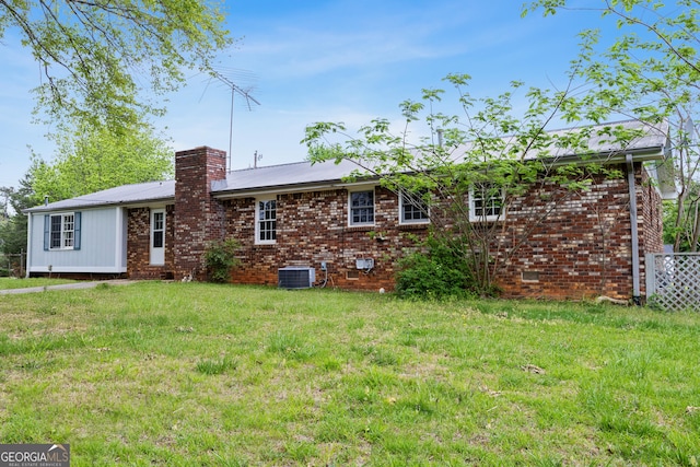 back of house featuring a lawn, brick siding, central air condition unit, and metal roof