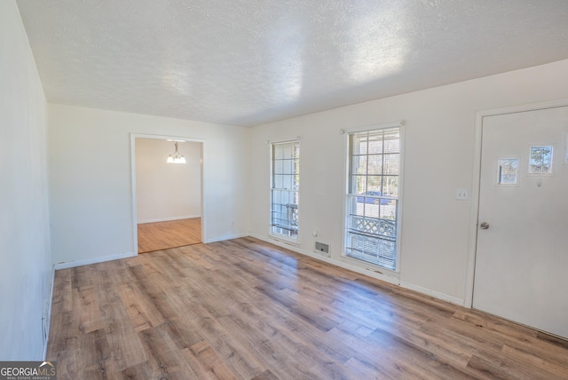 interior space featuring wood finished floors, a textured ceiling, baseboards, and a notable chandelier