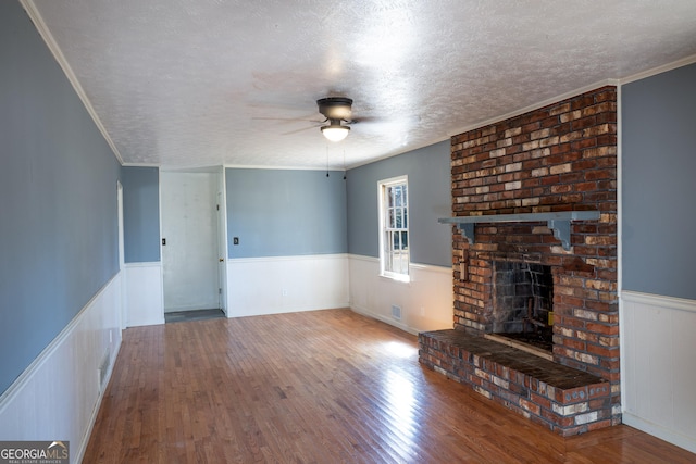 unfurnished living room with a wainscoted wall, a textured ceiling, wood finished floors, ceiling fan, and a fireplace