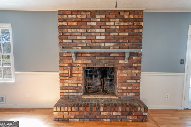 interior details with a brick fireplace, wood finished floors, visible vents, and ornamental molding