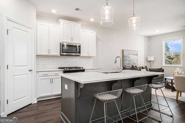 kitchen featuring tasteful backsplash, dark wood-style flooring, a kitchen island with sink, stainless steel appliances, and a sink