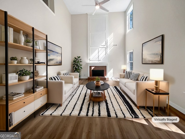 living room with a high ceiling, a fireplace, wood finished floors, and a ceiling fan