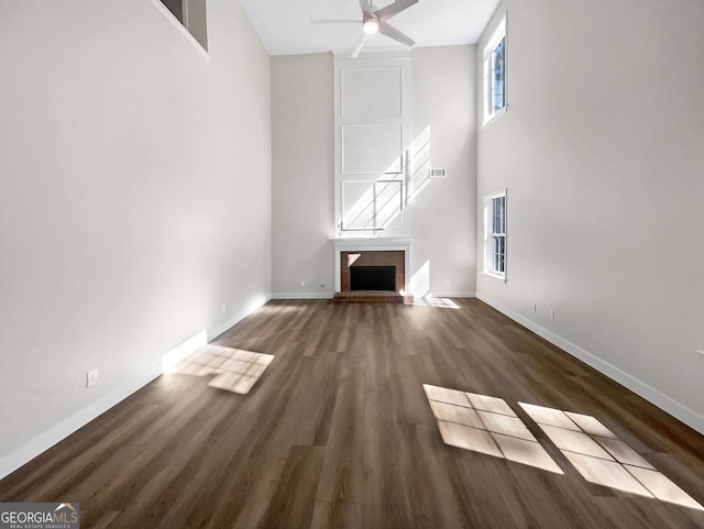 unfurnished living room featuring a high ceiling, a brick fireplace, ceiling fan, wood finished floors, and baseboards