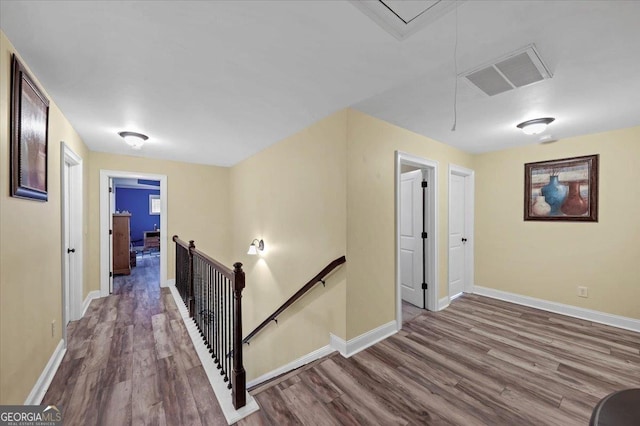 hallway featuring attic access, baseboards, visible vents, wood finished floors, and an upstairs landing