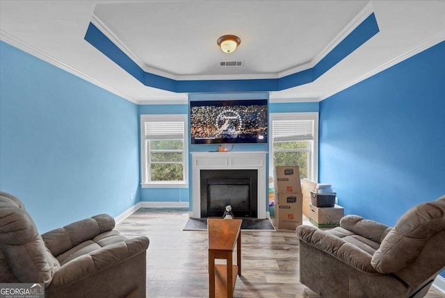 living room with a fireplace with flush hearth, a raised ceiling, a healthy amount of sunlight, and wood finished floors