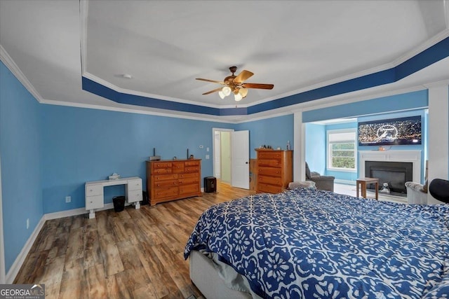 bedroom featuring baseboards, ornamental molding, wood finished floors, a tray ceiling, and a fireplace