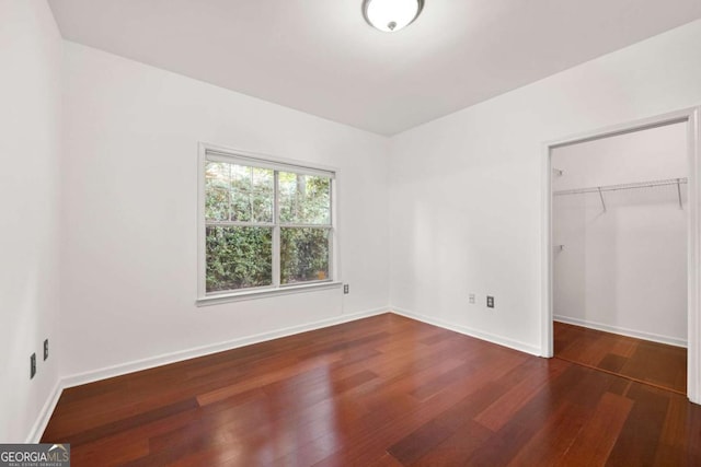 unfurnished bedroom featuring a closet, baseboards, a walk in closet, and wood finished floors