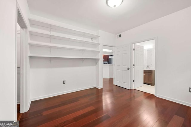 unfurnished bedroom with baseboards, visible vents, dark wood-style flooring, ensuite bathroom, and a spacious closet