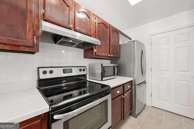 kitchen with light tile patterned floors, light countertops, decorative backsplash, appliances with stainless steel finishes, and under cabinet range hood