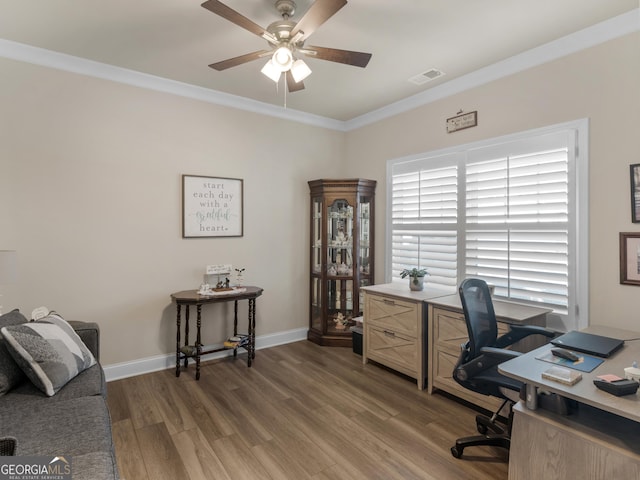 home office with crown molding, visible vents, light wood-style floors, ceiling fan, and baseboards