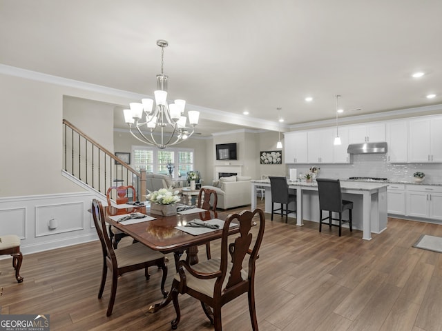 dining space with crown molding, a fireplace, wood finished floors, and a decorative wall