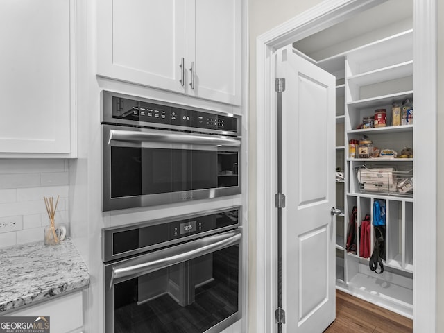 kitchen featuring light stone counters, wood finished floors, double oven, white cabinetry, and backsplash