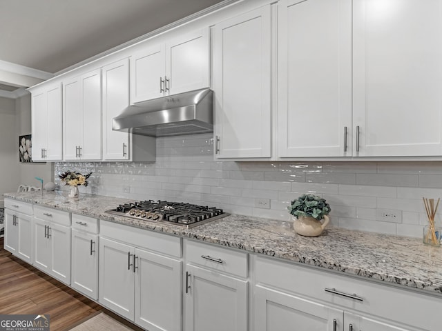 kitchen with under cabinet range hood, wood finished floors, white cabinets, tasteful backsplash, and stainless steel gas stovetop