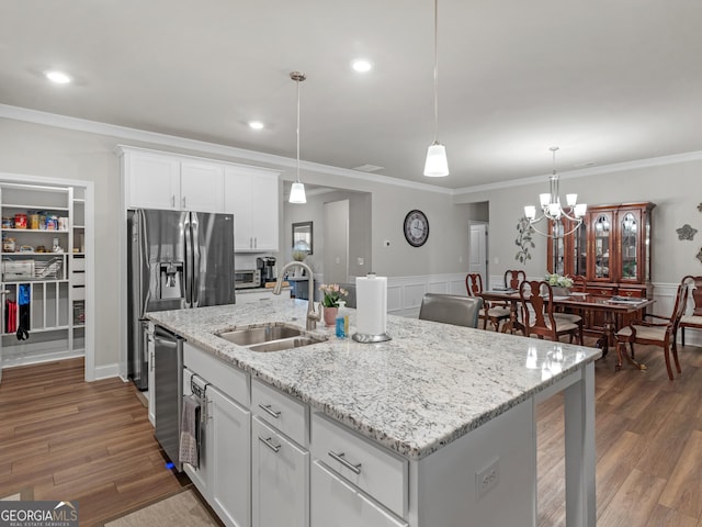 kitchen with pendant lighting, a wainscoted wall, white cabinets, a sink, and wood finished floors