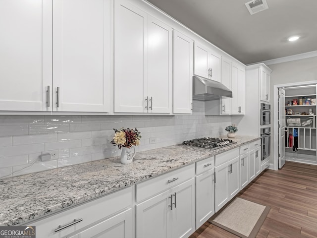 kitchen featuring under cabinet range hood, stainless steel appliances, wood finished floors, visible vents, and white cabinets