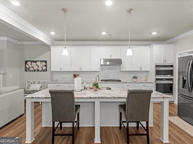 kitchen featuring under cabinet range hood, stainless steel appliances, a sink, and wood finished floors