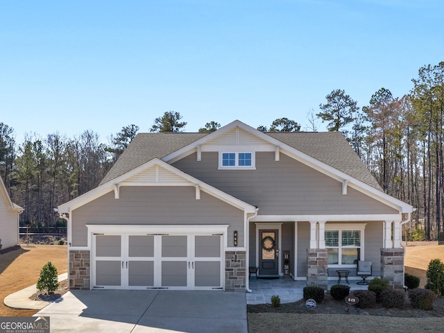 craftsman house featuring a garage, covered porch, a shingled roof, stone siding, and concrete driveway