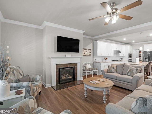 living area featuring crown molding, dark wood finished floors, a ceiling fan, a glass covered fireplace, and baseboards