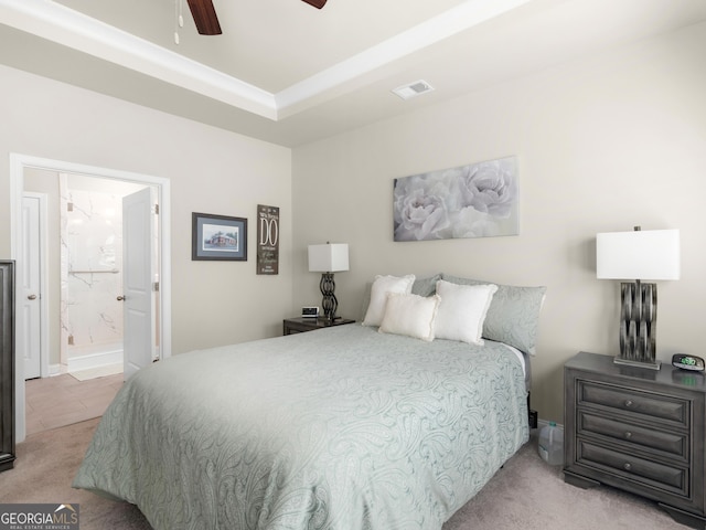 carpeted bedroom featuring ceiling fan, connected bathroom, visible vents, and a tray ceiling