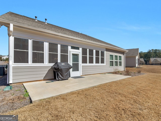 rear view of property with central air condition unit, a patio area, a lawn, and roof with shingles