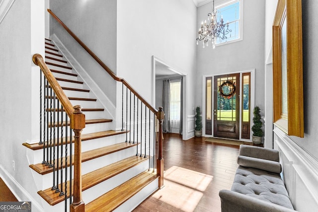 entrance foyer featuring stairs, hardwood / wood-style floors, a towering ceiling, and an inviting chandelier